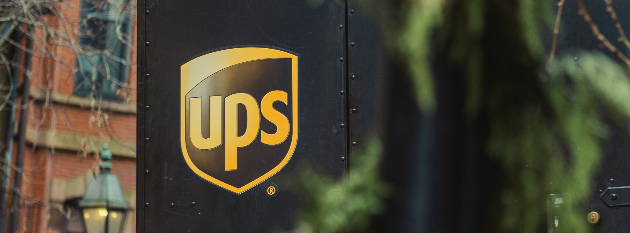 The back of a black UPS van, on the right side truck door is a golden UPS logo.
